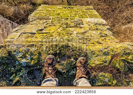 Tourist standing on high stone wall. Hiking shoes detail. Travelling theme. Sunset light.
