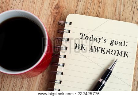 Today's goal - Be awesome text on notepad with pen and a cup of coffee, wooden background