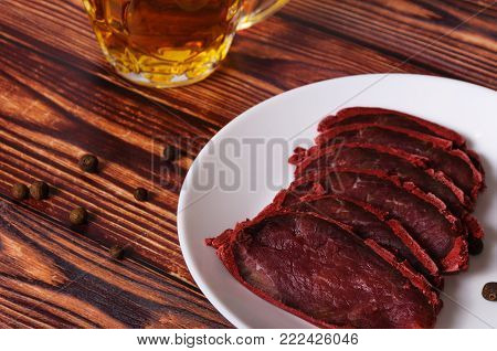 Fresh basturma on a white plate with a glass of beer on a wooden background.