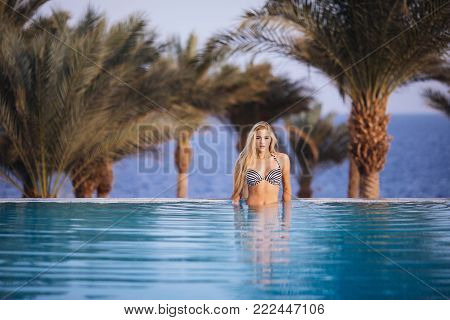 Luxury Resort. Woman Relaxing In Infinity Swimming Pool Water. Beautiful Happy Healthy Female Model