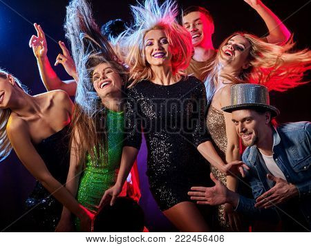 Dance party with group people dancing. Women and men have fun in night club. Happy girl with tousled hair on foreground. Back light on girls hair. Rest after hard day at work.