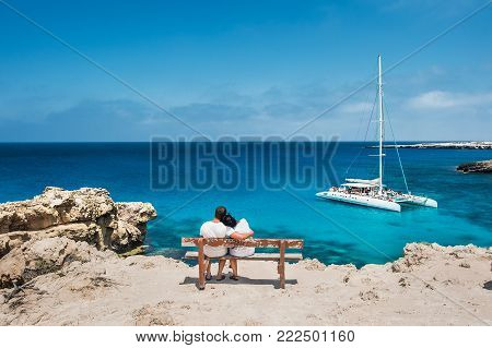 Loving couple sitting on a bench and looks at the lagoon. Honeymoon lovers. Man and woman on the island. Couple in love on vacation. A voucher for a cruise trip. Sea tour. Honeymoon trip. Cruise ship