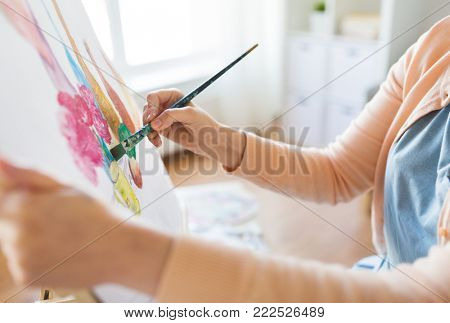 art, creativity and people concept - hands of artist with paint brush and easel painting still life on paper at studio