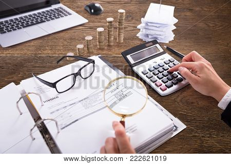 Close-up Of A Businessperson's Hand Analyzing Bill With Magnifying Glass At Workplace