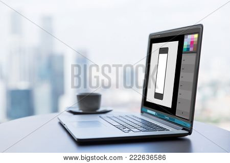 technology and design concept - laptop computer with smartphone image in graphics editor on table at office