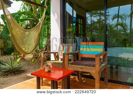 Chillout terrace zone near tropical hotel room with hammock and wooden chairs