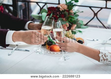 Weddings toast. glasses with champagne drink in bride and groom hands. Happy newlyweds drinking at ceremony. Loving couple created new family. Decorated alcohol drinks