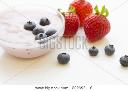 Healthy Breakfast Concept with a bowl of fresh homemade youghurt with blueberries and strawberries on white, close up, copy space