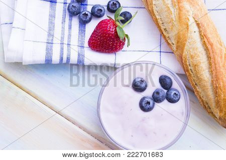 Romantic French or Rural Breakfast with a baguette, homemade youghurt and fresh blueberries and strawberry. Napkin and wood as a background, top view