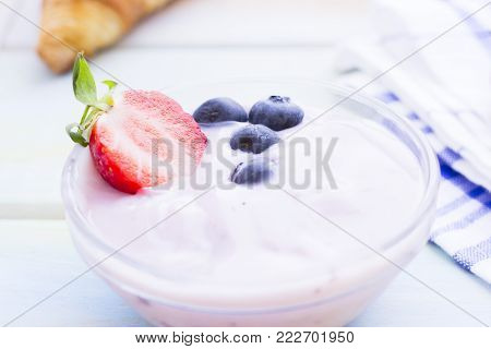 Delicious Healthy Breakfast with youghurt and fresh blueberries and strawberry on a white table, close up