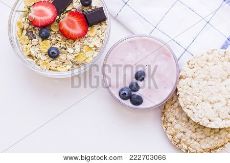 Healthy Breakfast Concept with homemade youghurt, wheat breadcrisps and a bowl of cereal with fresh berries and chocolate, top view. White background with a napkin