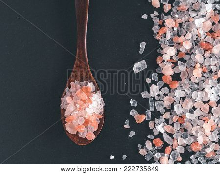 Himalayan pink salt in spoon on black stone background. Copy space