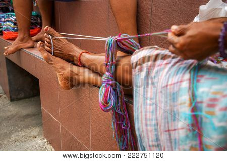 tanned legs of an old authentic Indonesian woman at work. The legs of an ordinary Asian woman hold the thread for knitting.