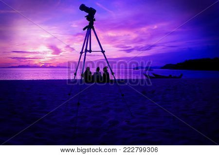 Silhouette camera and tripod with three girls sitting watching the sunrise on the beach at ang thong beach.Thailand