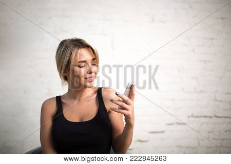 Confident woman web content writer reading publication on web page via mobile phone, standing in modern interior near copy space for your advertising. Hipster girl chatting on portable cell telephone