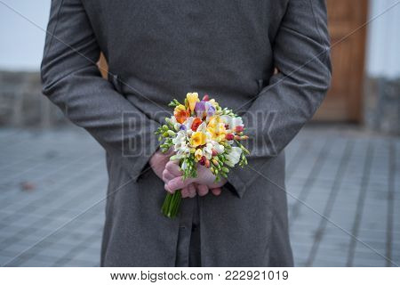 Man holding rose hiding on back at the park. Womans / Valentines Day concept.