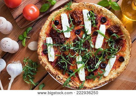 Gluten-free grain-free vegetarian pizza made from mashed cauliflower and almond flour, topped with sundried tomatoes, olives, goat cheese and fresh arugula. Top view.