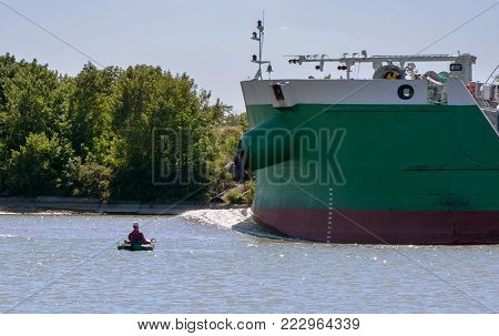 The fisherman on the fishing boat floats next to a big ship