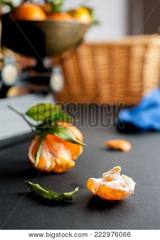 A bunch of fresh juicy clementines with green leaves in a scalepan and on a black table