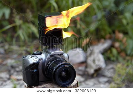 Digital Slr Camera With A Zoom Lens And A Burning Electronic On-camera Flash. Flames On The Flash Of