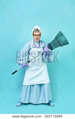 Cleaning Lady Fun. Elderly Funny Housewife Fooling Around With A Broom. Full Body Isolated Blue
