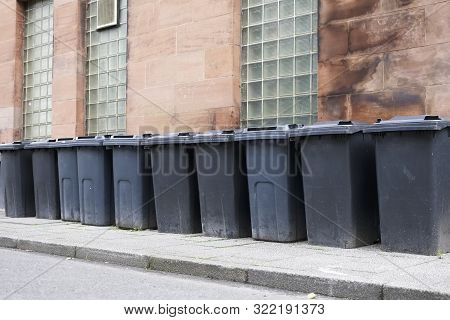 Black Wheelie Bins In A Row On Street With House Numbers Printed On Front Waiting For Bin Men To Col