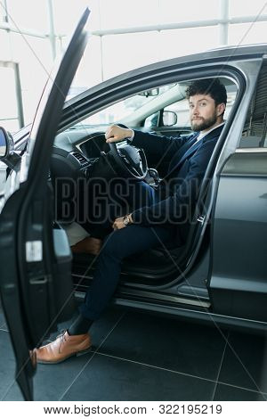 Happy Car Owner At The Dealership. Handsome Young Men Sitting At Front Seat Of The Car