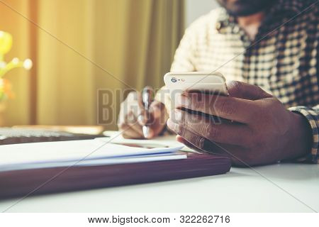 Casual Business Man Using Mobile Smart Phone Working, Taking Note, Schedule On Paper Notebook, Readi