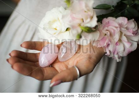 Female Hands Holding Two Yoni Eggs For Vumfit, Imbuilding Or Meditation Are Made From Pink Quartz An
