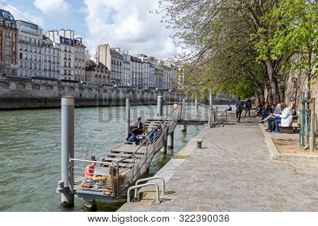 Paris, France, April 1, 2017: Quay at the edge of the canal with walkers. Geode in the background. Villette Park. Tourists walking near by Pont Neuf. The oldest bridge across the Seine river