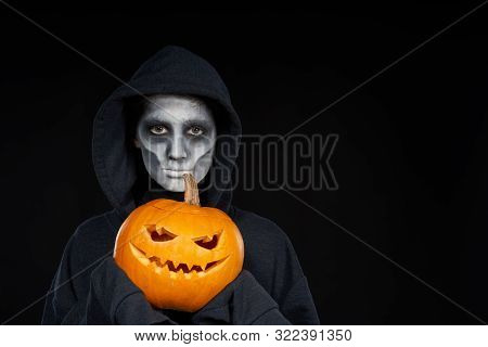 Boy With Halloween Makeup Holding Jack Olantern Pumpkin On Black Background