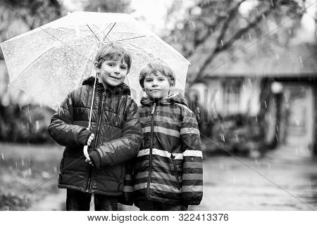 Two Little Kid Boys On Way To School Walking During Sleet, Rain And Snow With Umbrella On Cold Day. 