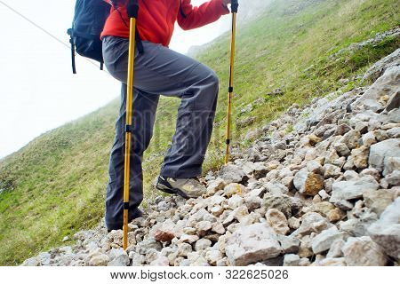 Female Hiker Going Up On A Mountain Trail With Trekking Poles