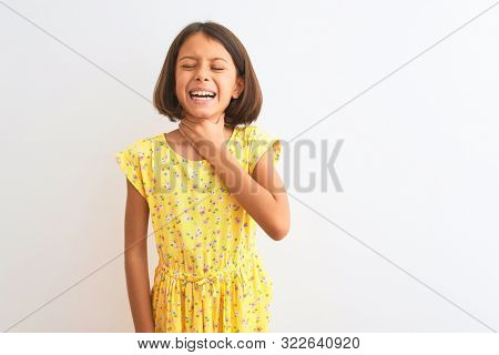 Young beautiful child girl wearing yellow floral dress standing over isolated white background Touching painful neck, sore throat for flu, clod and infection