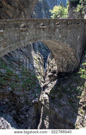 View Of A Wild River In The Viamala Gorge With Old Historic Stone Bridge In The Swiss Alps
