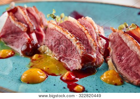 Macro shot of Sliced duck breast with hummus and plum sauce on turquoise plate. Exquisite serving restaurant main course with grilled goose fillet steak, greens and spices