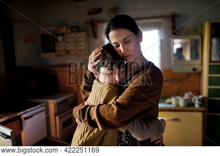 Portrait Of Sad Poor Mature Mother Hugging Small Daughter Indoors At Home, Poverty Concept.