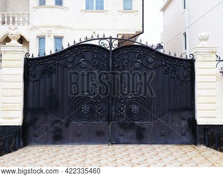 Black Gates With A Wrought-iron Pattern Of Monograms Adjoin The White Columns Of The Fence That Encl