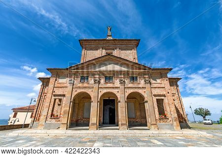 Low angle view of old brick catholic church under blue sky in small town of Diano d'Alba in Piedmont, Northern Italy.
