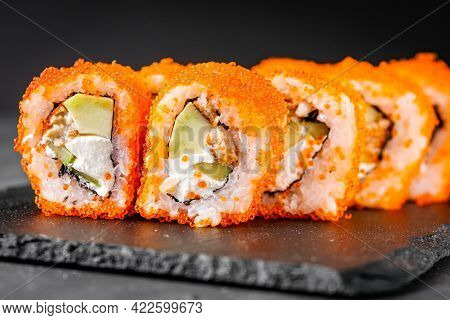 Appetizing Sushi Roll California With Eel Cheese Cucumber Avocado And Caviar Masago On A Black Stone
