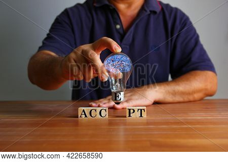 Man Holding Light Bulb With Illustration Of Brain In Hand With Text Accept On Wood Block. The Adopti