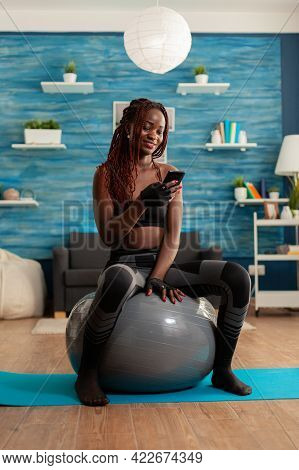 Active Athletic Black Woman Chatting On Smartphone Sitting On Swiss Ball In Home Living Room, After 
