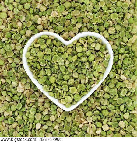 Roasted green peas healthy food in a heart shaped dish and forming a background. High in dietary fibre, protein, vitamins and minerals and has heart health benefits. Flat lay, top view.