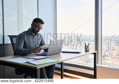 Indian Latin Focused Financier Sitting At Desk Doing Paperwork Working With Bank Taxes, Loans, Debit