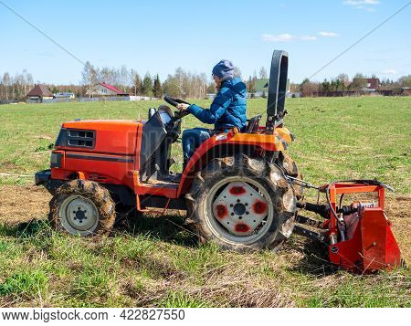 The Girl Sits In A Small Tractor And Drives Through The Field Mulching Grass. Land Cultivation, Agro