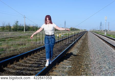 Teenage Girl In Jeans Walks On The Rails Of Railway And Keeps Balance With Her Hands.