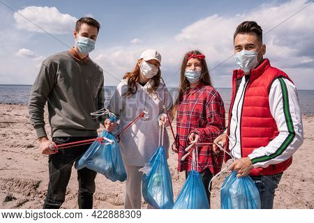 Young Volunteers In Medical Masks Holding Trash Bags And Grabbers Outside, Pick Up Trash Concept.
