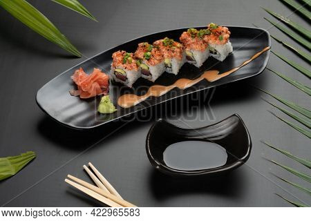 Sushi Roll - Maki Sushi made of tuna, avocado, mayonnaise and ebiko sushi isolated on black table with tropical leaves