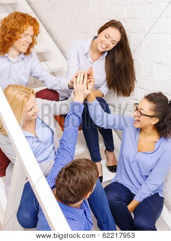 business, office, gesture and startup concept - smiling creative team doing high five gesture sitting on staircase