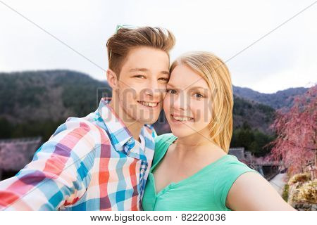 travel, tourism, technology, people and love concept - smiling couple with smartphone or camera taking selfie over asian village landscape background